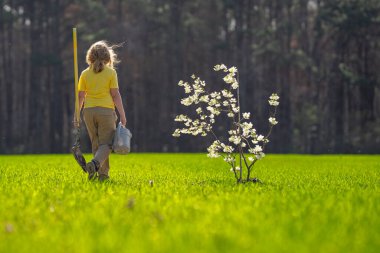 Çocuk bahçeye bir ağaç dikti. Çocuk kürek ve bitki ağacıyla toprak kazıyor. Çocuk bahçıvan meyve ağaçlarıyla ilgileniyor. Çocuklarla ağaç dikmek. Çocuklar için bahçe işleri. Kürek ağacı olan çocuk