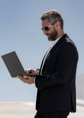 İş adamı dışarıda dizüstü bilgisayar kullanıyor. Olgun iş adamı dizüstü bilgisayar kullanıyor. Dizüstü bilgisayarı olan kendine güvenen bir iş adamı. İnternette iş. İş adamı laptoptaki verileri kontrol ediyor. Takım elbiseli iş adamı internette çalışıyor.