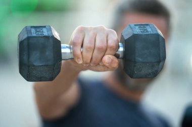 Olgun bir adamın dambılları dışarı kaldırırken yakın çekimi. Olgun adamların kol kasları halter egzersizi yapıyor. Kol halterine yakın çekim. Dambılı formda bir erkek kolunun yakın çekimi.