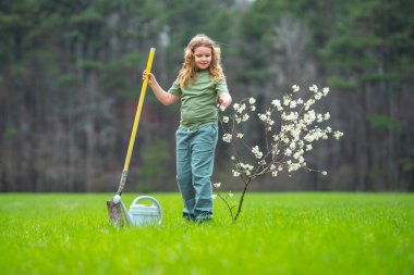 Bahçeye çocuk dikme ve sulama ağacı. Ağaç dikmenin bahar etkinliği. Kürek ve su bidonlarıyla çocuk işi. Çocuk meyve ağacı dikiyor. Bahçıvan çocuklar. Çocuk yetiştirme ve ağaç bakımı