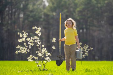 Bahçede çalışan bir çocuk. Bahçede yetişen ağaç ve bakım bitkisi. Bahçıvanlık sezonu. Bitki yetiştiren bir çocuk. Bahçe işleri. Çocuk bahçede meyve ağacı suluyor. Çocuk dikme ağacı. Bahçede bahar
