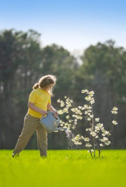 Çocuk bahçeye ağaç dikiyor. Çocuk kürekle toprak kazıyor ve ağaç dikiyor. Çocuk bahçıvan meyve ağaçlarıyla ilgileniyor. Çocuklarla ağaç dikmek. Yeşillik arayan bir çocuk. Çocuklar için bahçe.