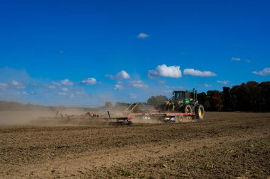 Traktör tarlada toprak sürüyor. Mavi gökyüzüyle tarlada toprak. Kırsal tarım arazilerinde traktör. Tarım traktörü toprakta çalışıyor. Çekici tarla sürme çiftliği. Çiftlik arazisi