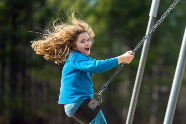 Çocuk parkta salıncakta sallanıyor. Sarı saçlı küçük bir çocuk salıncakta sallanıyor. Salıncakta gülümseyen mutlu çocuk. Mutlu çocukluk anları. Çocuk dışarıda oynuyor. Çocuk salıncakta eğleniyor. Çocuklar için açık hava oyunu