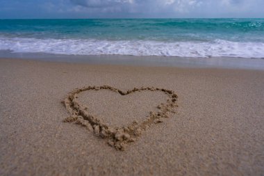 Kalp kumda çizilmiş. Dalgalar kalp şeklinde bir işaret oluşturuyor. Kumsalda aşk. Romantik yaz. Kumdan yapılmış bir kalp. Aşk ve okyanus dalgaları