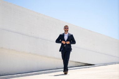 Dışarıda yürüyen bir iş adamı. Takım elbiseli başarılı bir iş adamı, tam boy. Takım elbiseli kendine güvenen bir iş adamı. İşadamı çekip gidiyor. Zarif takım elbiseli zengin adam. Kendine güvenen şehirli iş adamı.