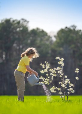 Bahçede ağaç yetiştiren bir çocuk. Çocuk kürekle toprak kazıyor ve ağaç dikiyor. Çocuk bahçıvan meyve ağaçları yetiştiriyor. Çocuklarla ağaç yetiştirmek. Çocuklar için bahçe işleri. Kürekli çocuk ağaç yetiştiriyor.