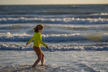 Mutlu çocuk yaz denizinde su sıçratarak oynuyor. Yaz tatili. Çocuk denizde dalgalarla oynuyor. Küçük çocuk denizde oynuyor ve su damlaları sıçrıyor. Çocuk denizde su sıçratmaca oynuyor. Yaz tatili