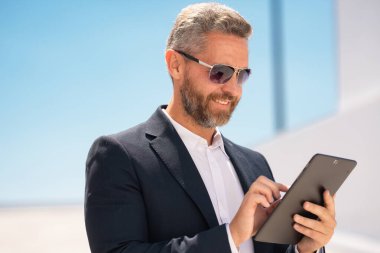 Açık havada tablet kullanan mutlu bir iş adamı. Tabletle başarılı bir iş adamı. Dışarıda tablet üzerinde çalışan bir iş adamı. Zarif iş adamı tableti kontrol ediyor. Dijital aygıt kullanan işadamı