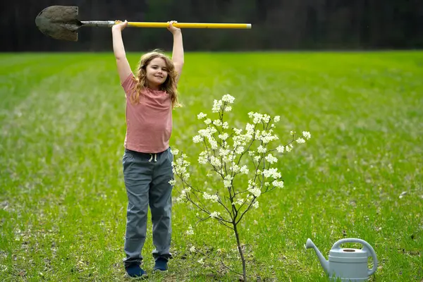 Çocuk dışarıda ağaç dikiyor. Bitkilerin bahar etkinliği. Çocuk kürek ve su bidonuyla çalışıyor. Çocuk meyve ağacı dikmiş. Bahçıvan çocuklar. Çocuk yetiştirme bitkisi ve ağaç bakımı. Kırsal çocuk hayatı