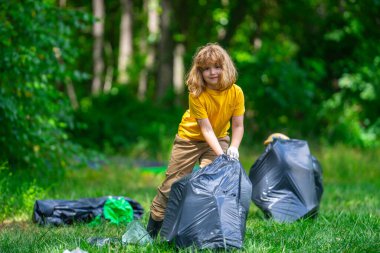 Lastik eldivenli çocuk çöp torbasıyla ormandaki çöpleri temizliyor. Eko, çevre koruma. Kirliliği geri dönüştür. Çocuk çöp ve plastik çöp topluyor. Çevreyi koru. Eko çocuklar