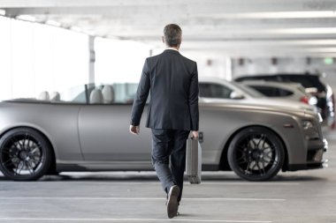 Lüks bir arabanın yanında zengin bir işadamı. Takım elbiseli zengin bir iş adamı. Şehirdeki başarılı zengin iş adamı. Kendine güvenen bir iş adamı. Başarı işi. İş adamı sokakta yürüyor