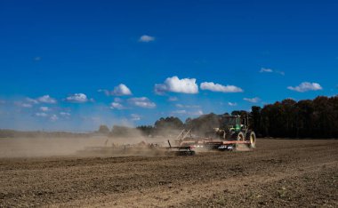 Traktör tarlada toprak sürüyor. Mavi gökyüzüyle tarlada toprak. Kırsal tarım arazilerinde traktör. Tarım traktörü toprakta çalışıyor. Çekici tarla sürme çiftliği. Çiftlik arazisi