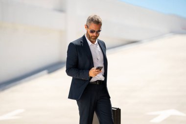 İş portresi. İş adamı dışarıda telefonla konuşuyor. Başarılı bir lider. Takım elbiseli adam dışarıda telefonda konuşuyor. İş adamı cep telefonunu tutar. Çantası olan bir iş adamı. İş başarısı. İş çağrısı