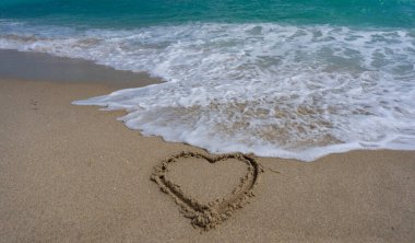 Deniz kumsalı. Manzaralı deniz sahili arkaplanı. Cennet okyanus manzarası. Kalp kumda çizilmiş. Dalgalar kalp şeklinde bir işaret oluşturuyor. Kumsalda aşk. Romantik yaz. Kumdan yapılmış bir kalp. Aşk ve okyanus dalgaları