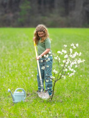 Çocuk dışarıda ağaç dikiyor. Bitkilerin bahar etkinliği. Çocuk kürek ve su bidonuyla çalışıyor. Çocuk meyve ağacı dikmiş. Bahçıvan çocuklar. Çocuk yetiştirme bitkisi ve ağaç bakımı. Doğadaki çocukluk.