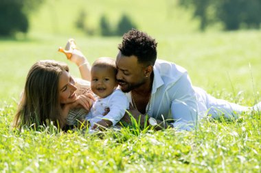 Çok ırklı ebeveynler ve parkta melez bir bebek. Dışarıda çok ırklı bir aile var. Bahçede melez bir bebek var. Çok ırklı bir aile. Çimlerde yatan çocuklu çok ırklı anne ve baba.
