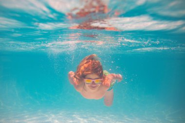 Yüzme havuzunda su altında bir çocuk. Çocuk su altında yüzüyor. Yüzme havuzunda su sıçratan çocuk. Aktif çocuklar sağlıklı yaşam tarzları, su altında yüzme. Çocukla yaz tatili. Çocuk su oyunu