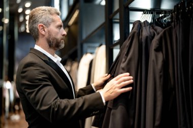 Klasik takım elbise. İspanyol bir işadamı iyi terzilikten ve takım elbiseden hoşlanır. İyi giyimli bir erkek model bir butikte poz veriyor. Perakende satış elemanı şık bir adamın mükemmel takımı bulmasına yardım eder.