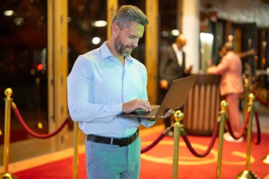 Gece sokakta dizüstü bilgisayar kullanan bir iş adamı. İş adamı dışarıda dizüstü bilgisayarda çalışmayı planlıyor. İşadamı, neon şehir ışıkları altında dizüstü bilgisayarda geziniyor. Serbest çalışan bir iş adamı. Gece işi.