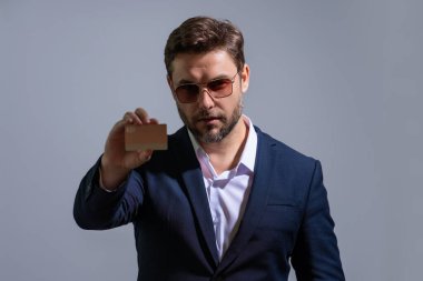 Elinde kredi kartı tutan yakışıklı bir adam. Gri stüdyo geçmişinde kredi kartı olan orta yaşlı bir adam. Kredi kartı konsepti. Takım elbiseli bir işadamı kredi kartıyla ödeme yapıyor.