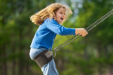 Bahar parkında sallanan neşeli çocuk. Sarı saçlı küçük bir çocuk salıncakta sallanıyor. Parkta gülümseyen mutlu çocuk. Mutlu çocukluk anları. Çocuk dışarıda oynuyor. Çocuk salıncakta eğleniyor. Çocuklar için açık hava oyunu