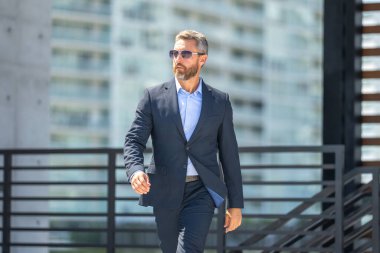 Başarılı bir iş adamı dışarıda yürüyor. Kendine güvenen bir iş adamı. Başarı işi. Takım elbiseli olgun iş adamı. Yakışıklı şirket lideri. Şehir ortamında zengin bir iş adamı. Şık bir iş ve lider.