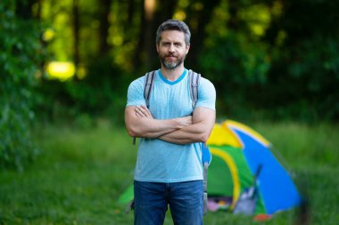 Gezgin doğada kamp yapmaktan hoşlanıyor. Doğaya yaz gezisi. Orman kampında dinlenen adam. Kamp gezisi. Yürüyüşten sonra çadırın yanında dinleniyor. Barışçıl bir kamp alanında özgürlük tatili. Yazın piknikteki adam