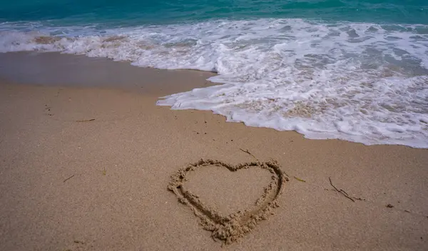 Deniz kumsalı. Manzaralı deniz sahili arkaplanı. Cennet okyanus manzarası. Kalp kumda çizilmiş. Dalgalar kalp şeklinde bir işaret oluşturuyor. Kumsalda aşk. Romantik yaz. Kumdan yapılmış bir kalp. Aşk ve okyanus dalgaları