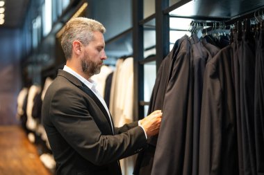 İş adamı için uygun. İyi giyimli bir erkek model bir butikte poz veriyor. Perakende satış elemanı şık bir adamın mükemmel takımı bulmasına yardım eder. Bir mağaza müdürü şık bir takım elbise ayarlar.