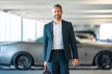 Lüks bir arabanın yanında zengin bir iş adamı. Takım elbiseli zengin bir iş adamı. Şehirdeki başarılı zengin iş adamı. Kendine güvenen bir iş adamı. Başarı işi ve zenginlik. İş adamı sokakta yürüyor