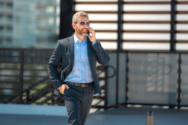 İş adamı yürüyor ve telefonla arıyor. Kendine güvenen bir iş adamının önemli bir çağrısı var. İş görüşmesi. Telefon görüşmesi. Patron telefonla konuşmakla meşgul. Zengin iş adamı. İş çağrısı