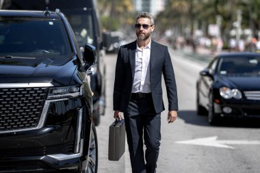 Olgun iş adamı. Zengin iş adamı başarının tadını çıkarıyor. Lüks bir iş. Pahalı arabanın önündeki zengin adam. Lüks iş seyahati. Klasik takım elbiseli, kendinden emin zengin bir iş adamı.