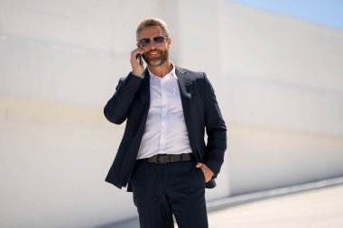 Ofis çalışanı dışarıda cep telefonuyla konuşuyor. Cep telefonunda iş adamı konuşması. İş adamı telefon görüşmesi yapıyor. Şık bir iş adamı telefon kullanıyor. İş görüşmesi. Meşgul işadamı telefonda konuşuyor.