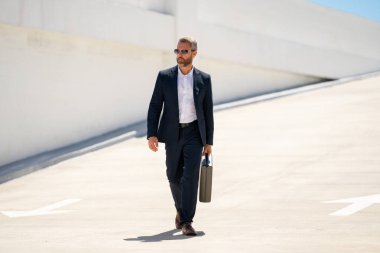 Açık hava iş portresi. Dışarıda yürüyen bir iş adamı. Başarılı lider hareket halinde. Çantalı takım elbiseli adam. İşadamı işe gidiyor. Çantası olan bir iş adamı. İş başarısı