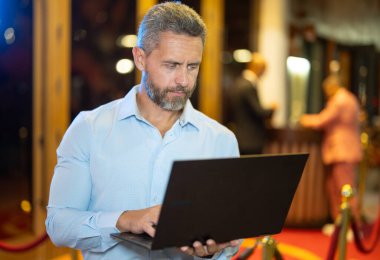 Gece sokakta dizüstü bilgisayar kullanan bir iş adamı. İş adamı dışarıda dizüstü bilgisayarda çalışmayı planlıyor. İşadamı, neon şehir ışıkları altında dizüstü bilgisayarda geziniyor. Serbest çalışan bir iş adamı. Gece işi.