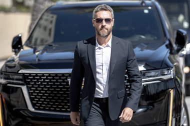 Dışarıdaki iş adamı. Zengin iş adamı başarının tadını çıkarıyor. Şık takım elbiseli lüks iş adamı. Pahalı arabanın önündeki zengin adam. Lüks iş seyahati. Klasik takım elbiseli, kendinden emin zengin bir iş adamı.