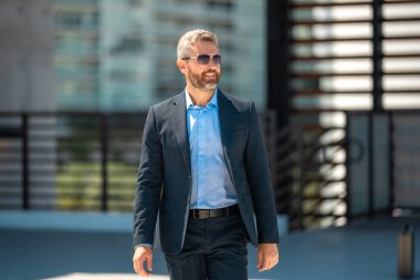 Başarılı bir iş adamı dışarıda yürüyor. Kendine güvenen bir iş adamı. Başarı işi. Takım elbiseli olgun iş adamı. Yakışıklı şirket lideri. Şehir ortamında zengin bir iş adamı. Şık bir iş ve lider.