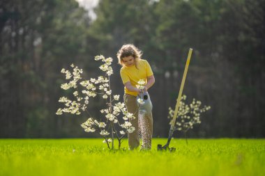 Çocuk bahçeye bir ağaç dikti. Çocuk kürek ve bitki ağacıyla toprak kazıyor. Çocuk bahçıvan meyve ağaçlarıyla ilgileniyor. Çocuklarla ağaç dikmek. Çocuklar için bahçe işleri. Kürek ağacı olan çocuk