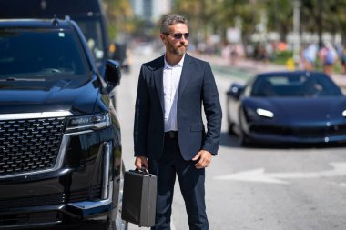 Başarılı bir iş adamı pahalı lüks bir arabanın yanında. Başarılı iş adamı. Takım elbiseli olgun iş adamı. Takım elbiseli zengin iş adamı dışarıda yürüyor. Lüks başarılı iş adamı. İş başarısı