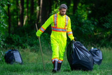 Üniformalı adam temizlik için çöp plastiği topluyor. Çöpleri toplayan adam. Çöp şişeleri toplandı. Plastik atık. Çöp toplama, çevre. Ekoloji, kirlilik, plastiklerden temizlik