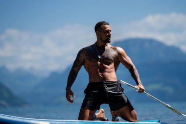 Seksi yaz erkeği. Suda ıslak kaslı erkek vücudu. Çıplak seksi erkek vücudu. İnsan yaz doğasında suya su sıçratır. Yaz plajında poz veren formda bir adam. Dağdaki gölde su sıçratan güçlü adam.