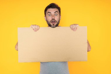 Yakışıklı, şaşkın bir adam elinde boş tahtayla stüdyoyu işaret ediyor. Kopyalama alanı olan boş tabela gösteren harika bir adam. Fikir ve teklif. Reklamınız. Boş reklam panosu