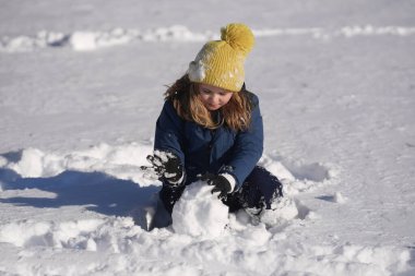 Çocuklar kış oyunu oynuyor. Çocuk kış şapkasıyla karda oynuyor. Sıcak giysili mutlu çocuk kar yağarken eğleniyor. İlk kar yağışında çocuk dışarıda karla oynuyor. Çocuklar için kış aktiviteleri
