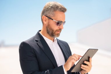 Ciddi bir iş adamı dışarıda tablet kullanıyor. Tabletle başarılı bir iş adamı. Dışarıda tablet üzerinde çalışan bir iş adamı. Zarif iş adamı tableti kontrol ediyor. Dijital aygıt kullanan işadamı