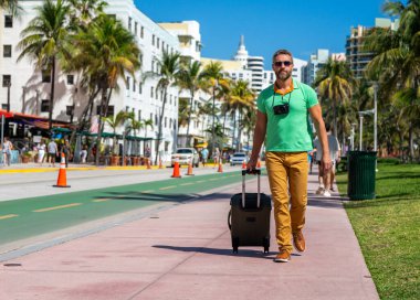 Miami 'nin güneşli sokaklarında bir turist yürüyor. Bir erkek turist, tropikal bir şehirde yaz tatilinin tadını çıkarır. Bavullu bir turist şehir manzarasını keşfediyor. Erkek turist şehirde yürüyor