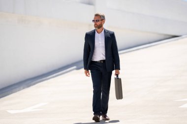 Açık hava iş portresi. Dışarıda yürüyen bir iş adamı. Başarılı lider hareket halinde. Çantalı takım elbiseli adam. İşadamı işe gidiyor. Çantası olan bir iş adamı. İş başarısı