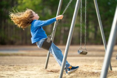 Çocuk parkta salıncakta sallanıyor. Sarı saçlı küçük bir çocuk salıncakta sallanıyor. Salıncakta gülümseyen mutlu çocuk. Mutlu çocukluk anları. Çocuk dışarıda oynuyor. Çocuk salıncakta eğleniyor. Çocuklar için açık hava oyunu