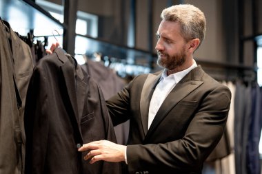 Bir butik danışmanı müşterinin mükemmel takımı bulmasına yardım eder. Lüks bir giysi koleksiyonu. Zarif takım iş adamı için mükemmel. İyi dikilmiş bir takım.