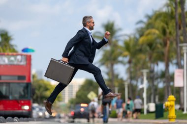 İş atlayışı. Caddeye atlayan bir iş adamı. Takım elbiseli bir işadamı geç kaldı ve atladı. Sıçrama hareketiyle meşgul bir iş adamı. Kendine güvenen işadamı heyecanla zıplıyor.